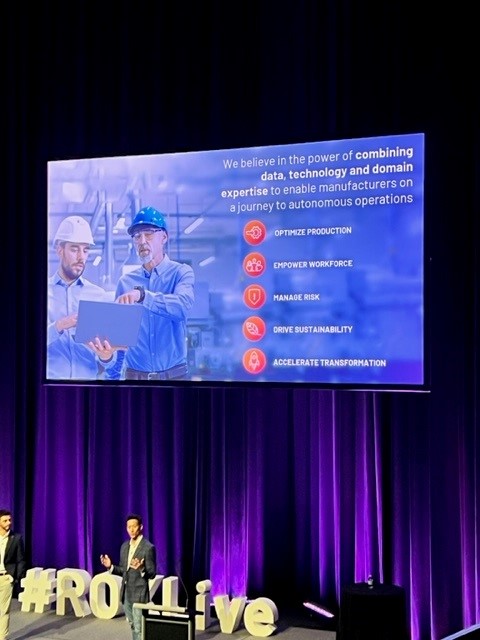 Man standing on a stage at the ROKLive 2023 event, with a powerpoint presentation playing in the background