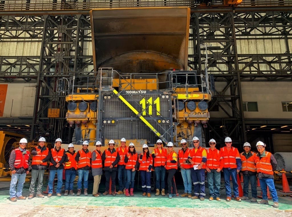 A group people in high vis gear standing in front of a large mine truck.