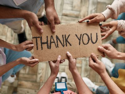 International Volunteer Day recognises the 1 billion people who volunteer around the world every day. This picture shows a number of pairs of hands holding a cardboard sign that says 'thank you.'