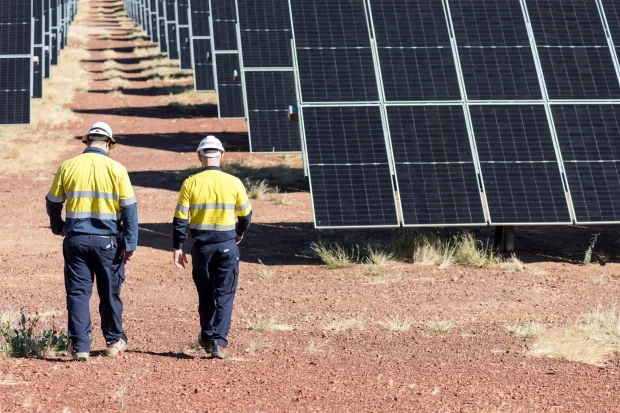 Two men wearing navy and yellow high vis walking toward some solar panels at Dugald River Solar Farm