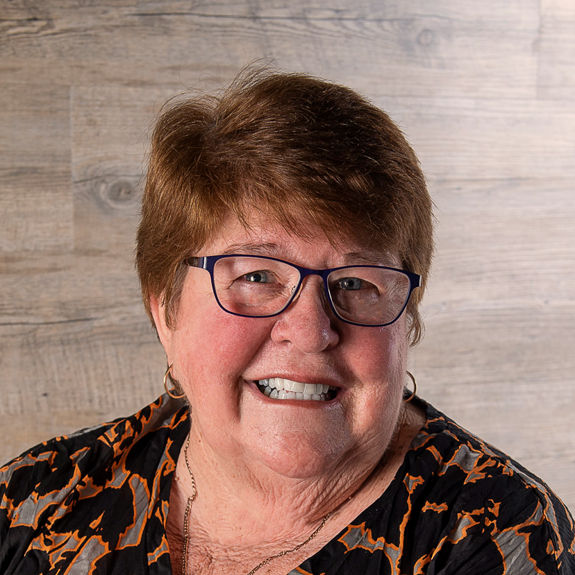 Profile photo of a smiling lady in glasses on a timber background