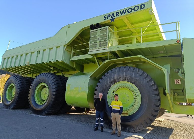 Two men standing at the wheel of a giant truck