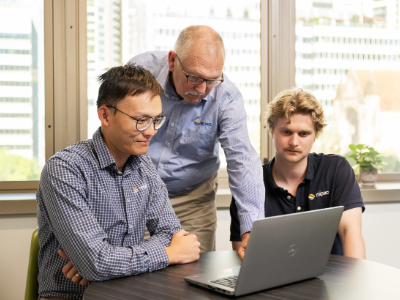 Three men, one older, two younger, looking at a computer screen together.